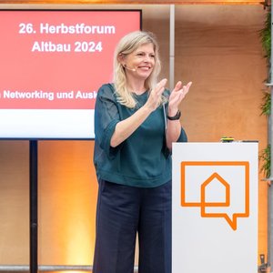 Natasha Walker steht auf der Bühne und moderiert das Herbstforum, eine Fachtagung für energetische Gebäudesanierung.