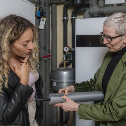 Energieberaterin prüft gemeinsam mit einer jungen Frau die Rohrdämmung der Heizung.