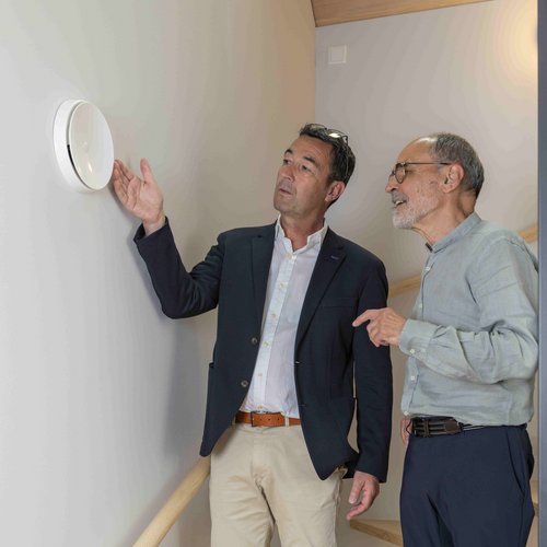 Ein Energieberater erklärt einem Mann die Funktionsweise der Lüftung. Sie stehen im Treppenhaus eines Gebäudes.