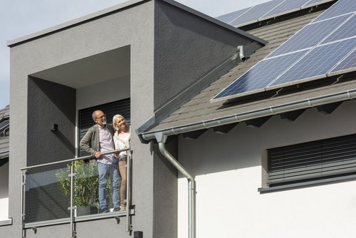 Bild zeigt ein Paar links im Bild, das auf einer Dachterasse steht. Sie schauen auf Photovoltaik-Module auf dem Dach, die sich rechts im Bild befinden.