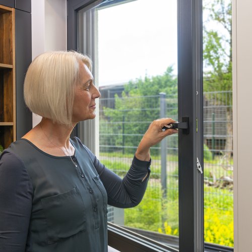 Frau hält einen Fenstergriff fest und öffnet das Fenster.