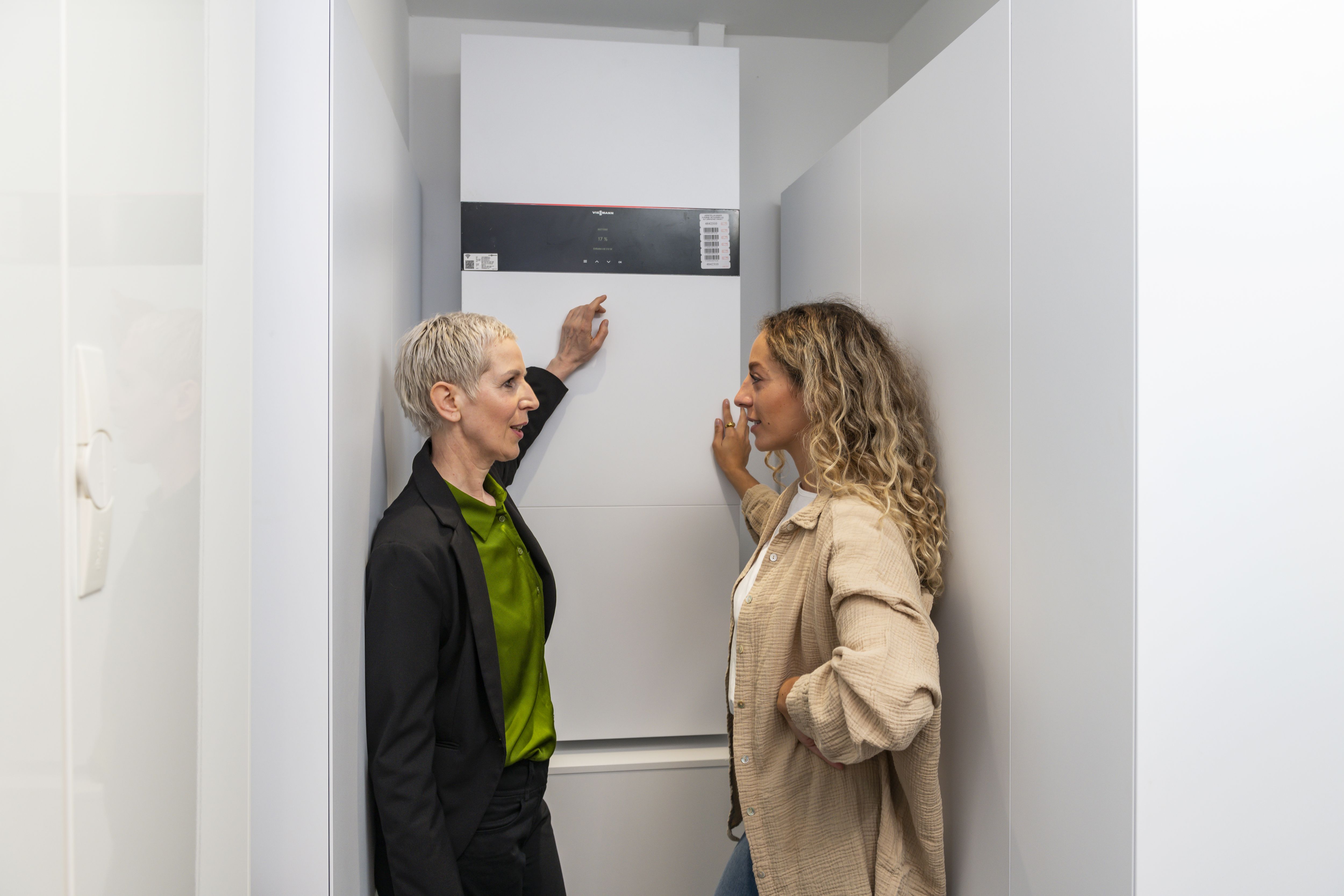 Das Foto zeigt zwei Frauen vor einem Solarstromspeicher. Die Frau links im Bild zeigt auf den Speicher und erklärt der Frau recht im Bild ihre Funktion.