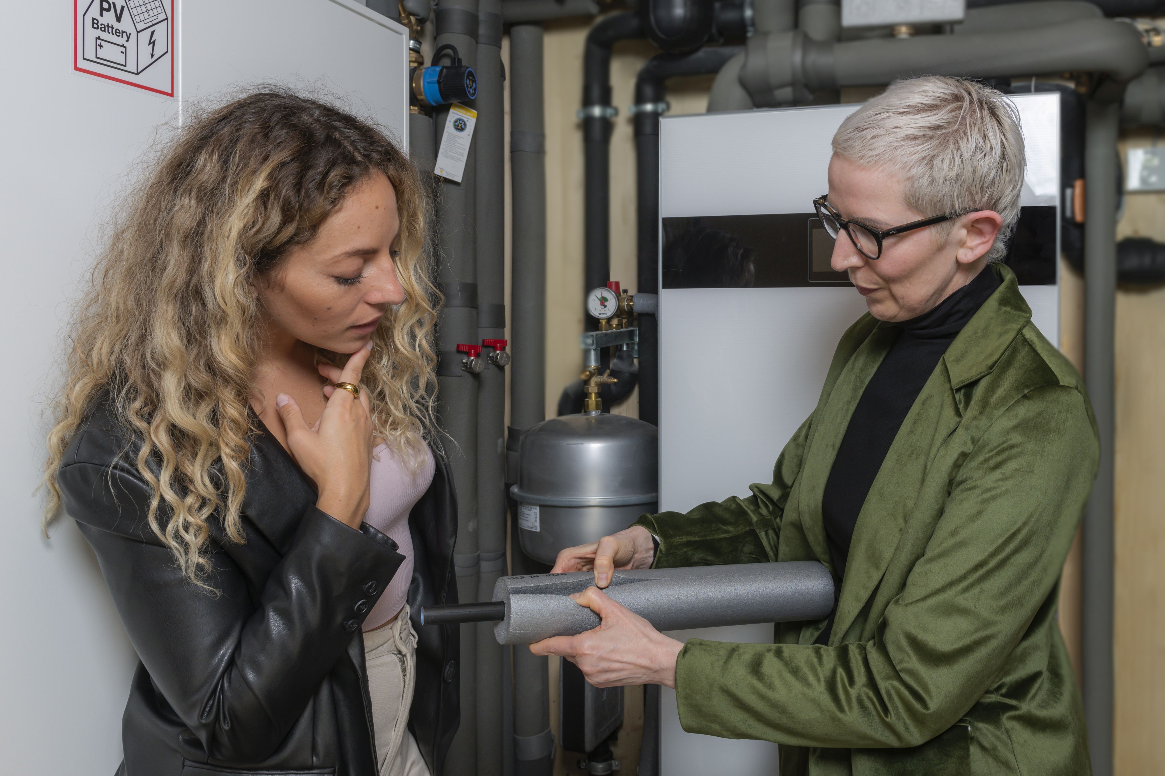 Energieberaterin prüft gemeinsam mit einer jungen Frau die Rohrdämmung der Heizung.