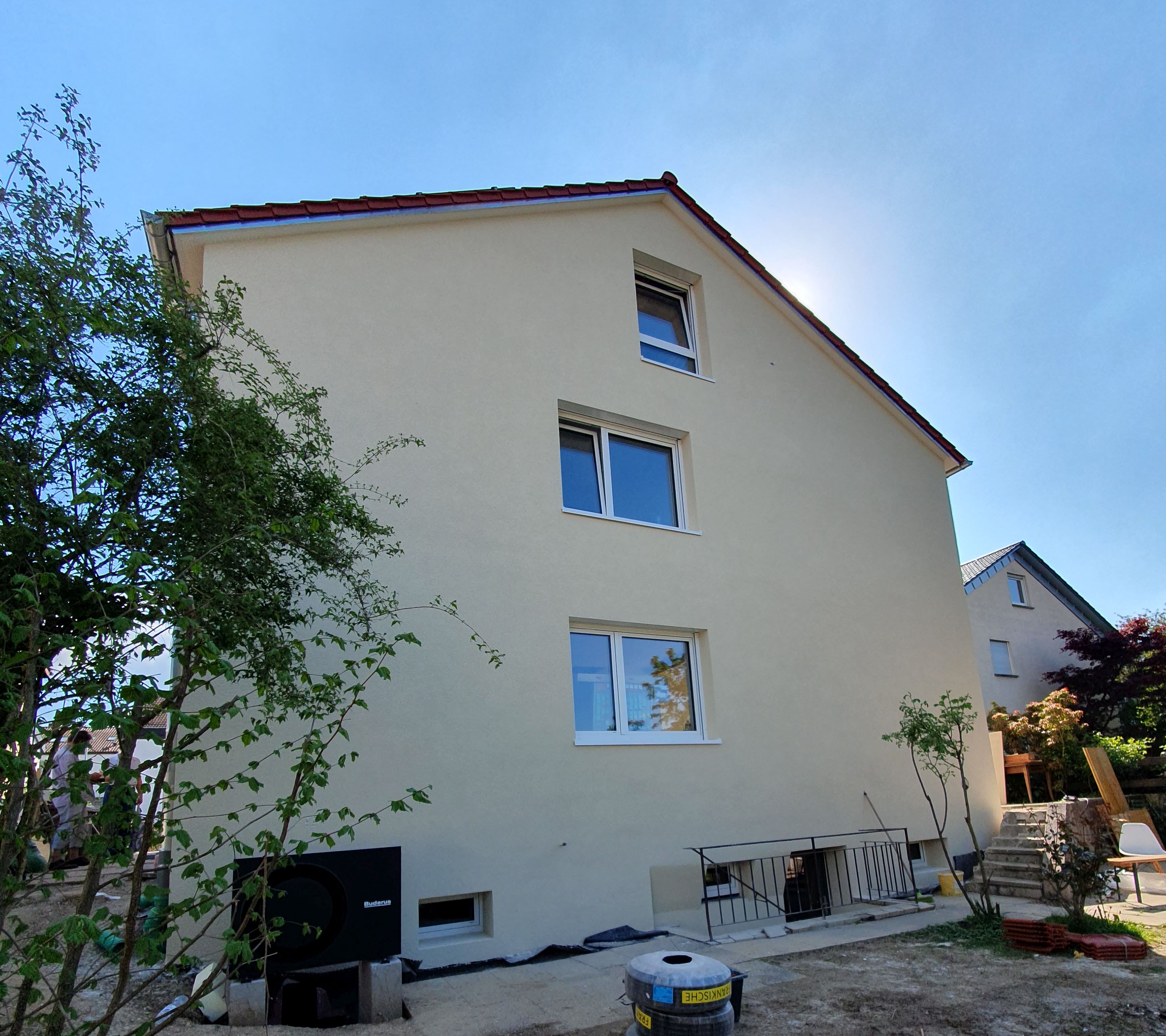 Das Bild zeigt ein fertig saniertes Haus von außen. Die Fassade ist gelb gestrichen. Links neben dem Haus steht eine Wärmepumpe.
