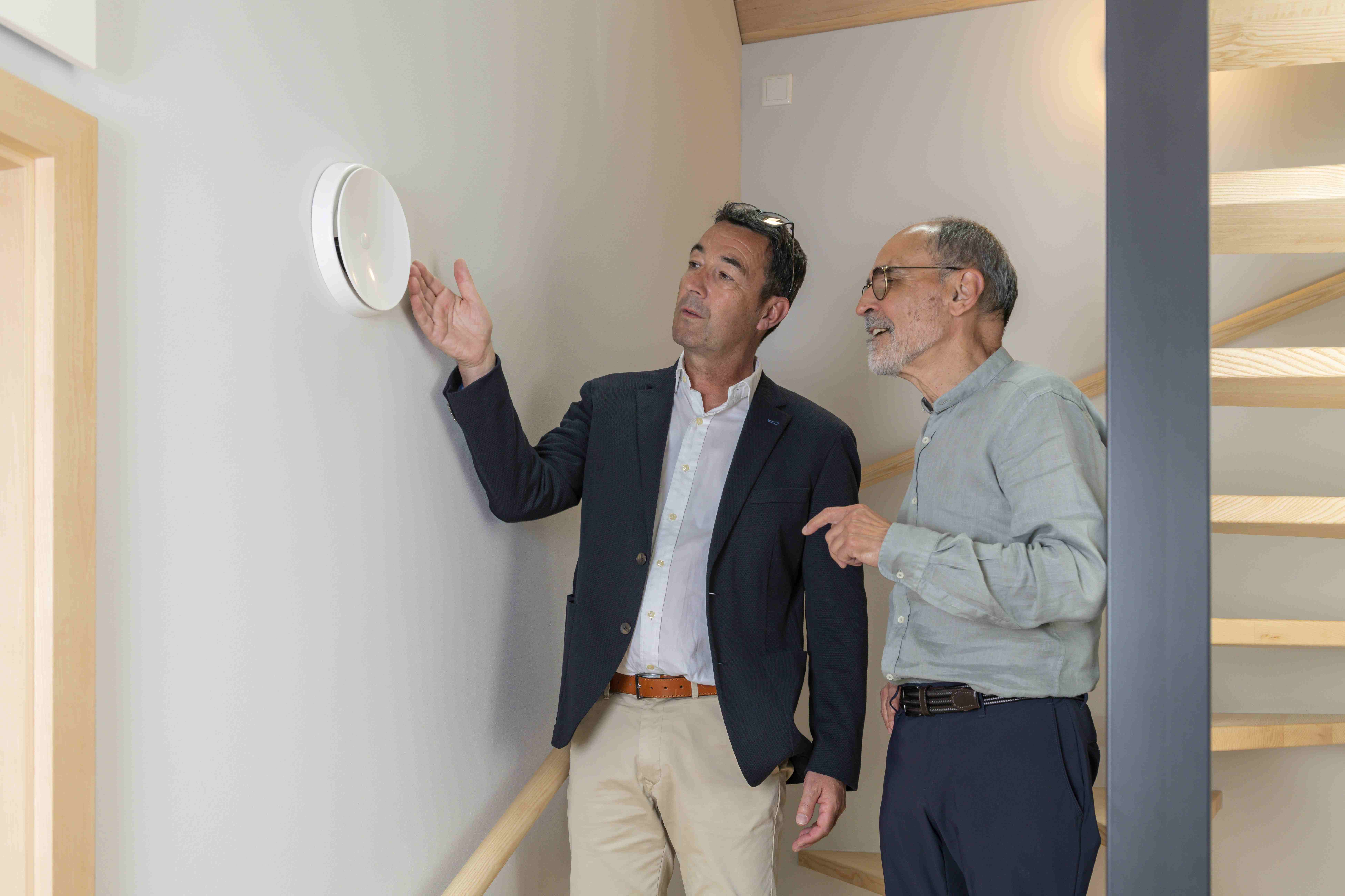 Ein Energieberater erklärt einem Mann die Funktionsweise der Lüftung. Sie stehen im Treppenhaus eines Gebäudes.